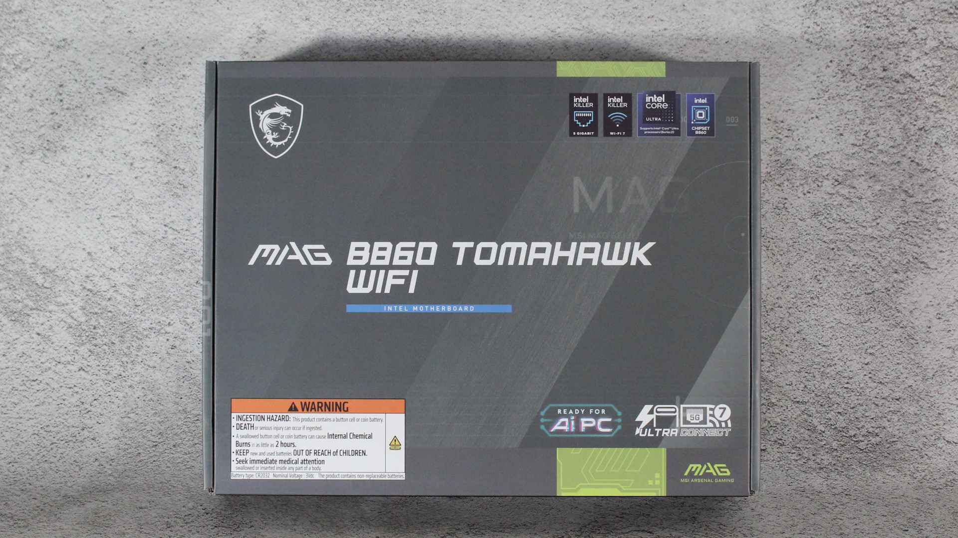 Плата MSI B860 Tomahawk Wifi находится в своей серой коробке на сером ковре. Логотип "готов к AI ПК" здесь может применяться к любой современной материнской плате, если вы планируете установить GPU.